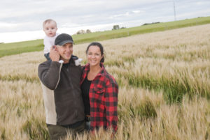 parents and an infant standing in a wheat field