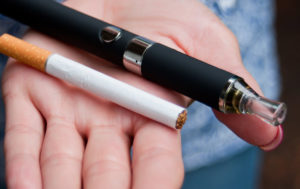 cigarette and vape pen held in the palm of a hand